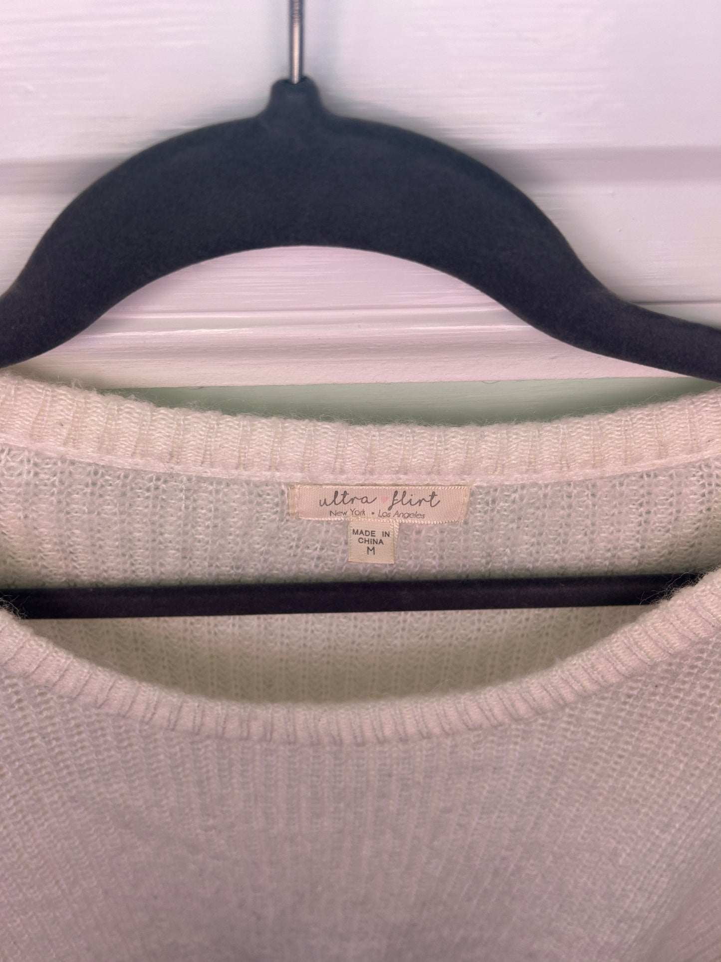 White knit sweater with colorful geometric patterned sleeves featuring green, black, purple, and mustard accents.