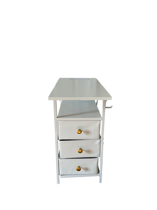 Compact white nightstand with three fabric drawers and gold knobs, featuring an open shelf and metal frame.