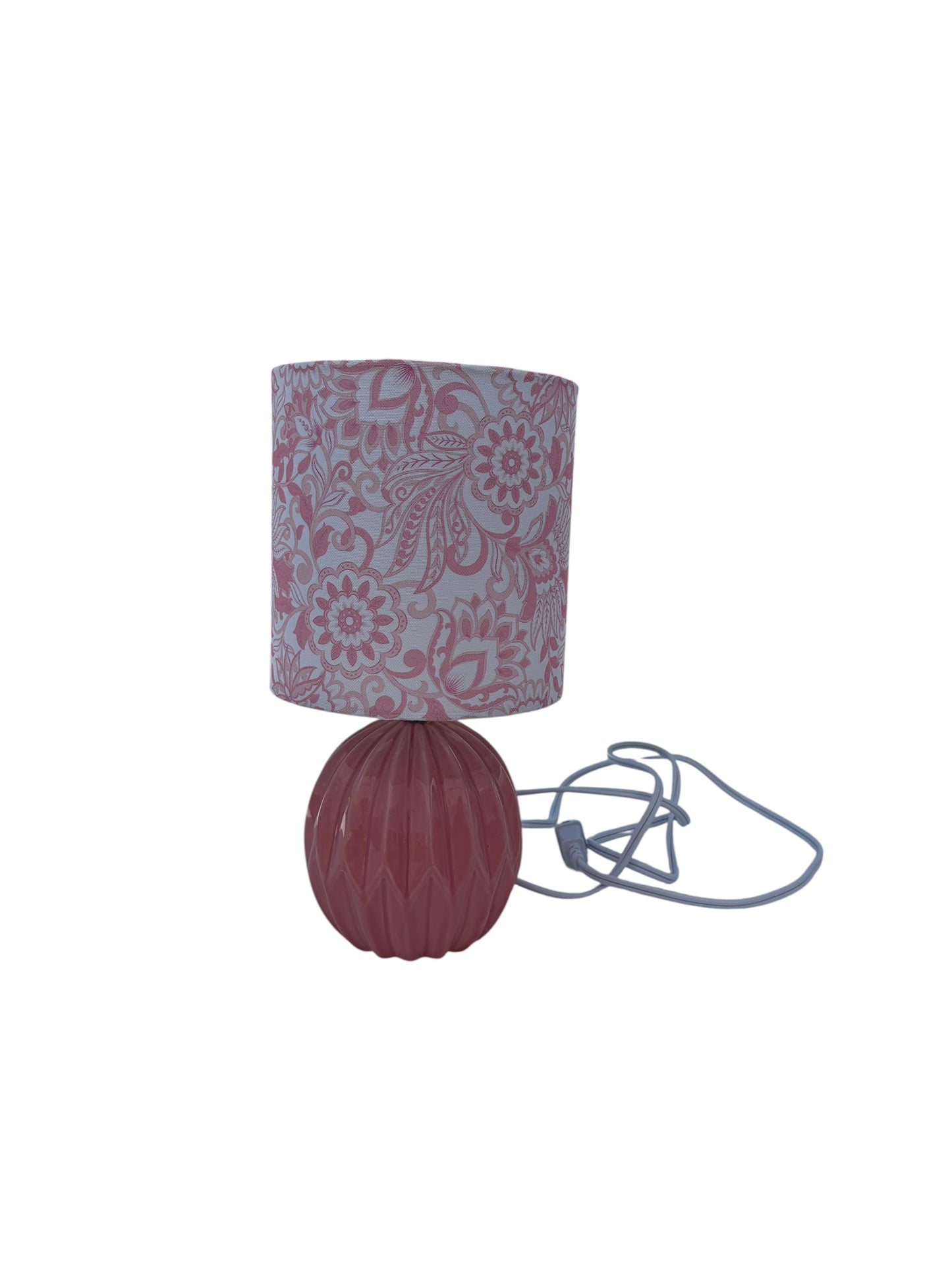 A pink table lamp with a floral patterned fabric shade and ribbed ceramic base.