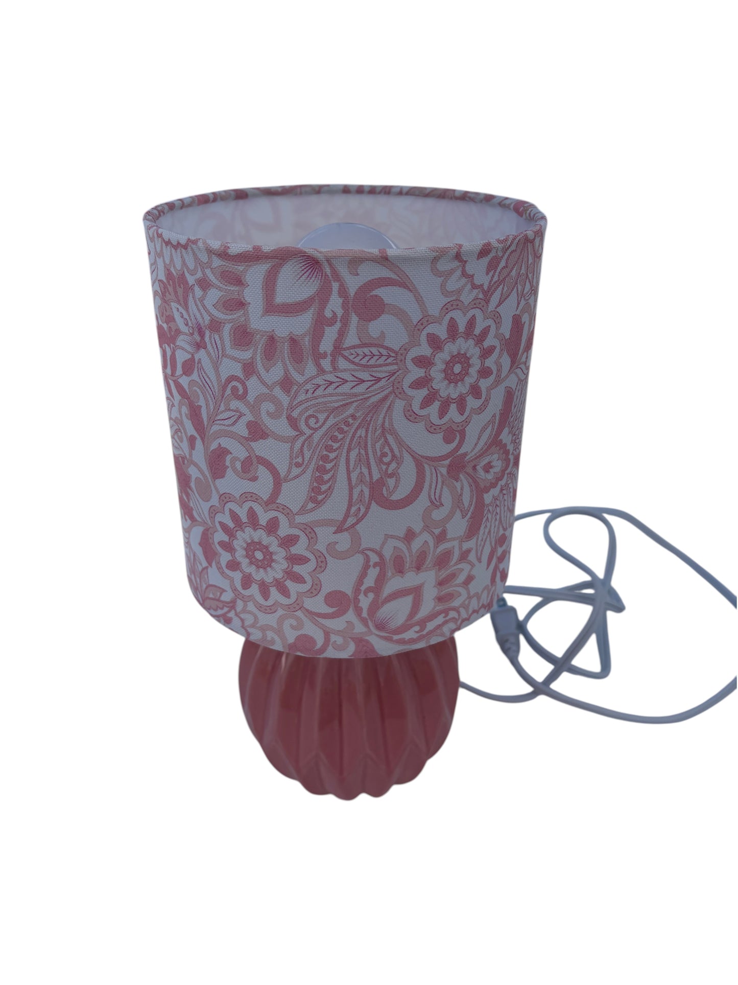A pink table lamp with a floral patterned fabric shade and ribbed ceramic base.